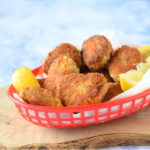 Kipnuggets Italian style 400 g kippendijfilets 50 gram zongedroogde tomaat 70 gram parmezaanse kaas, geraspt 2 el gehakte bieslook 1 tl knoflookpoeder 1 tl oregano versgemalen peper bloem ei panko (Japans broodkruim) zonnebloemolie Voor de pestomayonaise: 4 el mayonaise 1,5 el citroensap 1 el pesto Ook nodig: keukenmachine Snijd de kippendijen in stukken en halveer de zongedroogde tomaten. Doe alles in de keukenmachine, samen met 50 gram Parmezaanse kaas, de bieslook, knoflook, oregano en flink wat versgemalen peper. Pulseer net zo lang totdat je een (soort van) gladde massa hebt die aan gehakt doet denken. Pak nu drie diepe borden. Kluts in bord 1 het ei los, strooi in bord 2 een dikke laag bloem en strooi in bord 3 een flinke laag panko. Hussel de achtergehouden (20 gram) Parmezaanse kaas door de panko. Vorm nu nuggets van het kipmengsel. Zorg dat ze ongeveer even groot zijn, gebruik ongeveer een eetlepel per keer. Haal de nuggets door de bloem, dan het ei en dan de Parmezaan-panko. Leg de nuggets op een bord tot gebruik. Verhit in een wok een flinke laag zonnebloemolie. Bak de kipnuggets in delen goudbruin en gaar (keer ze halverwege). Het is echt belangrijk dat je niet teveel nuggets tegelijk bakt! Laat de gebakken nuggets uitlekken op keukenpapier. Klop de ingrediënten voor de pestomayonaise door elkaar en serveer dit bij de kipnuggets als dip.