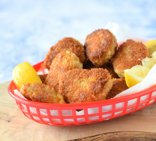 Kipnuggets Italian style 400 g kippendijfilets 50 gram zongedroogde tomaat 70 gram parmezaanse kaas, geraspt 2 el gehakte bieslook 1 tl knoflookpoeder 1 tl oregano versgemalen peper bloem ei panko (Japans broodkruim) zonnebloemolie Voor de pestomayonaise: 4 el mayonaise 1,5 el citroensap 1 el pesto Ook nodig: keukenmachine Snijd de kippendijen in stukken en halveer de zongedroogde tomaten. Doe alles in de keukenmachine, samen met 50 gram Parmezaanse kaas, de bieslook, knoflook, oregano en flink wat versgemalen peper. Pulseer net zo lang totdat je een (soort van) gladde massa hebt die aan gehakt doet denken. Pak nu drie diepe borden. Kluts in bord 1 het ei los, strooi in bord 2 een dikke laag bloem en strooi in bord 3 een flinke laag panko. Hussel de achtergehouden (20 gram) Parmezaanse kaas door de panko. Vorm nu nuggets van het kipmengsel. Zorg dat ze ongeveer even groot zijn, gebruik ongeveer een eetlepel per keer. Haal de nuggets door de bloem, dan het ei en dan de Parmezaan-panko. Leg de nuggets op een bord tot gebruik. Verhit in een wok een flinke laag zonnebloemolie. Bak de kipnuggets in delen goudbruin en gaar (keer ze halverwege). Het is echt belangrijk dat je niet teveel nuggets tegelijk bakt! Laat de gebakken nuggets uitlekken op keukenpapier. Klop de ingrediënten voor de pestomayonaise door elkaar en serveer dit bij de kipnuggets als dip.